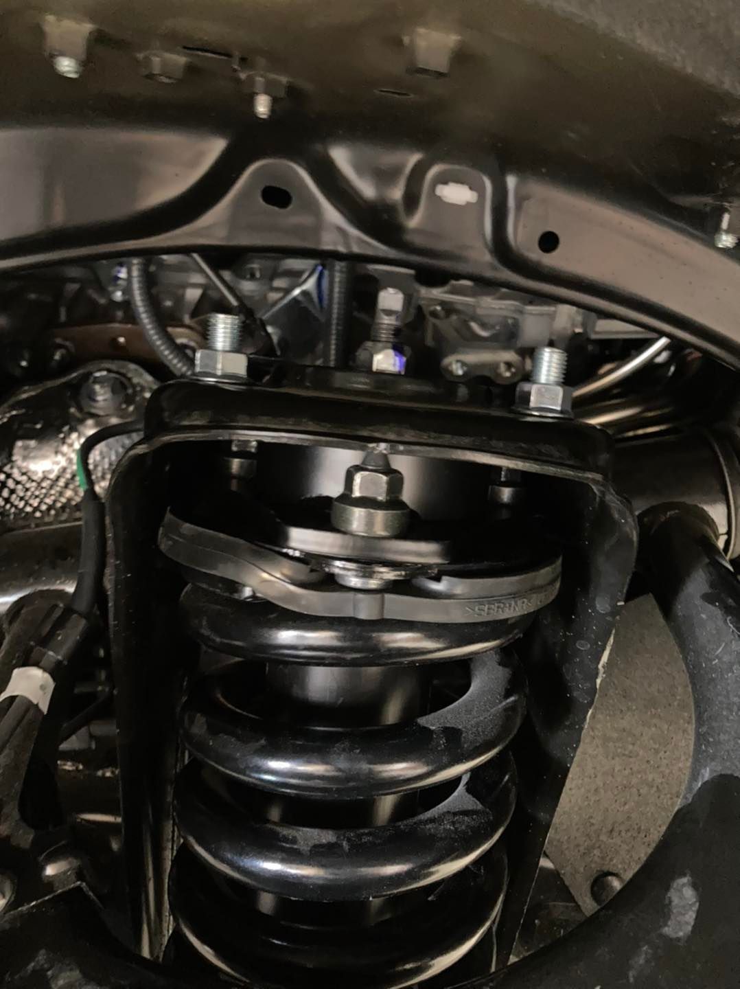 Black suspension system components, bolts, and coil spring assembly under a vehicle.