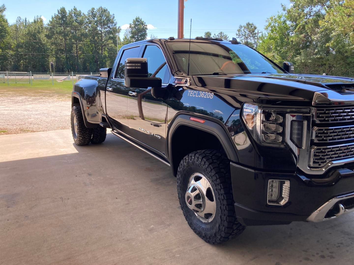Black GMC truck parked on concrete, glossy finish. Reflecting sun. Outdoor setting.