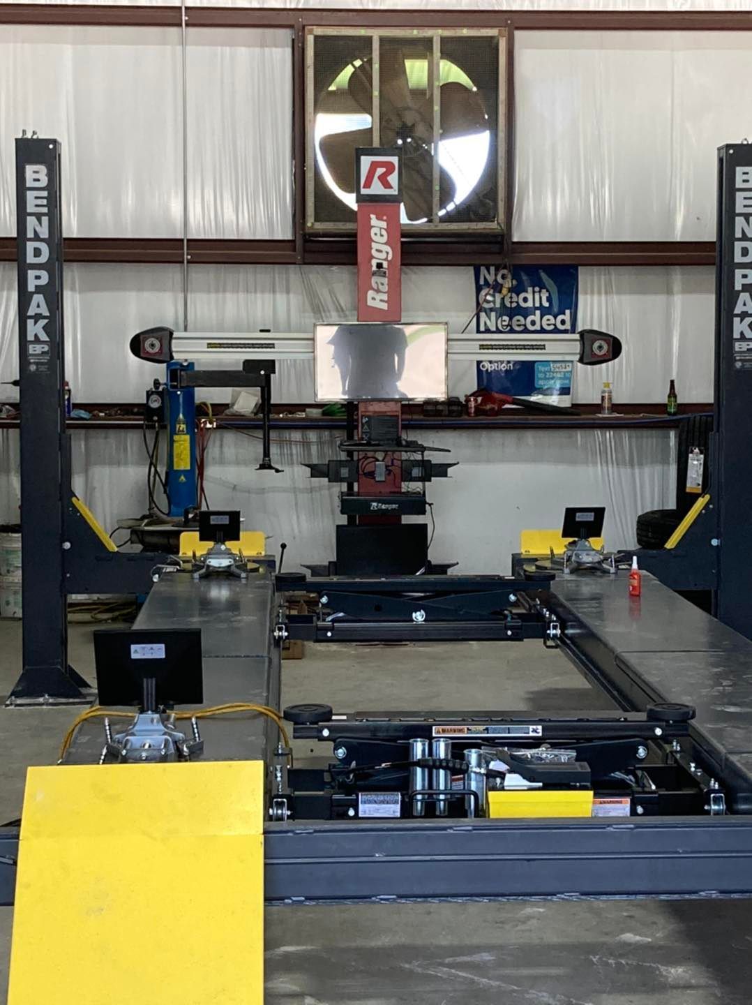 Car alignment machine in a garage; BendPak lifts, Hunter alignment system, fan, tools, and advertising signs.
