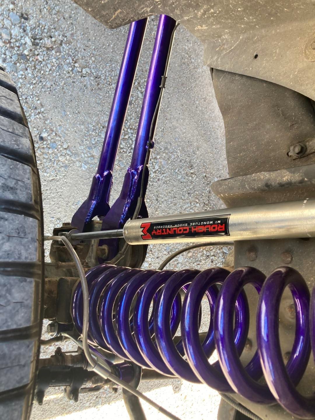 Purple suspension parts on vehicle. Coil spring, shocks, and support bars in a vehicle's wheel well.