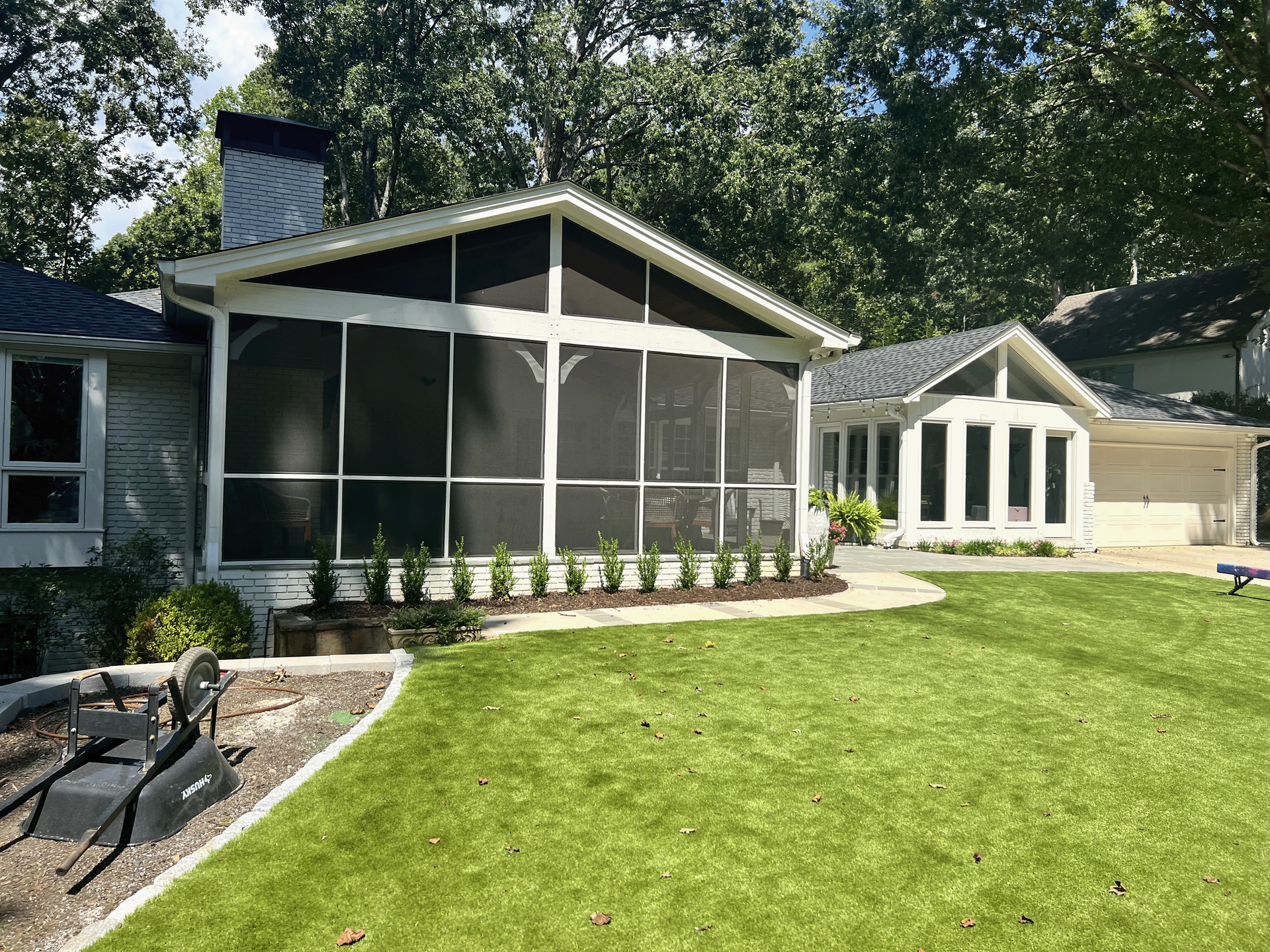 A house with a screened in porch and a large lawn in front of it.