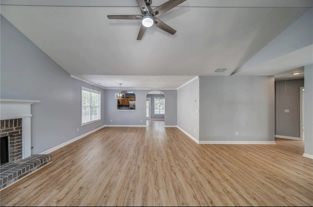 An empty living room with hardwood floors , a fireplace and a ceiling fan.