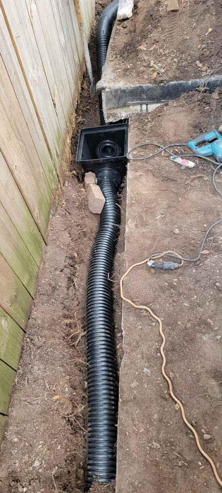 A black pipe is being installed in the ground next to a wooden fence.