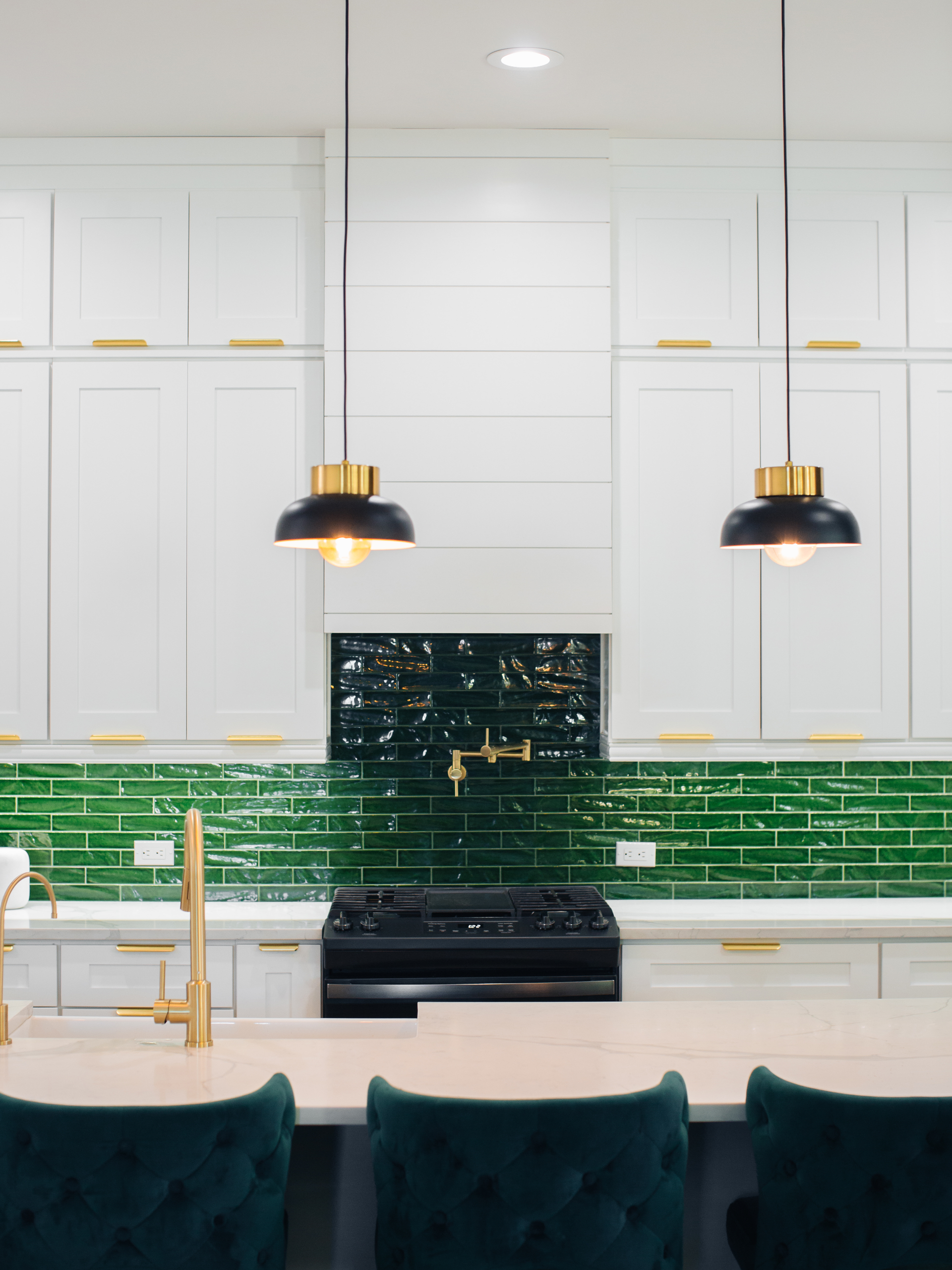 A kitchen with white cabinets , green tiles , a stove and a sink.