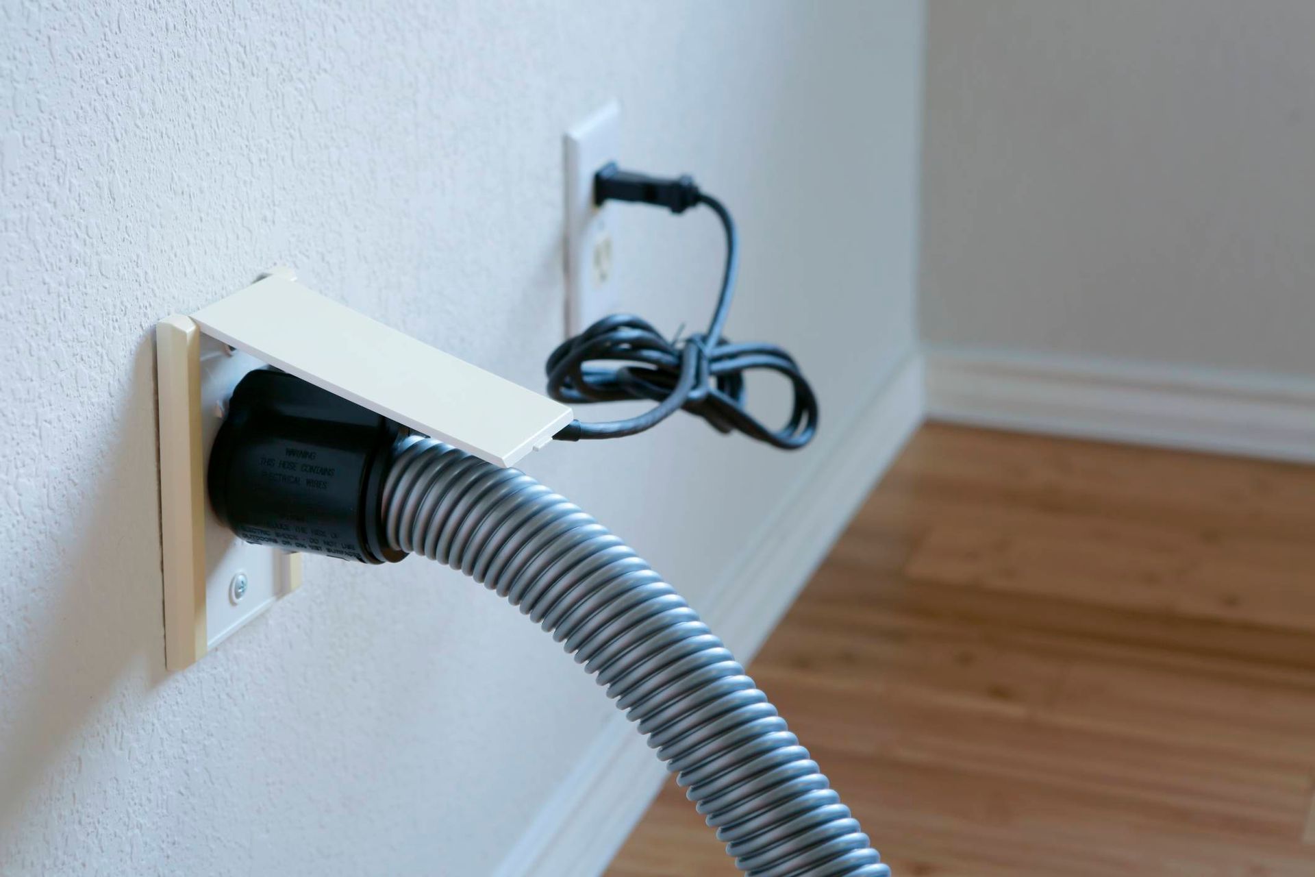 A vacuum hose is plugged into a wall outlet