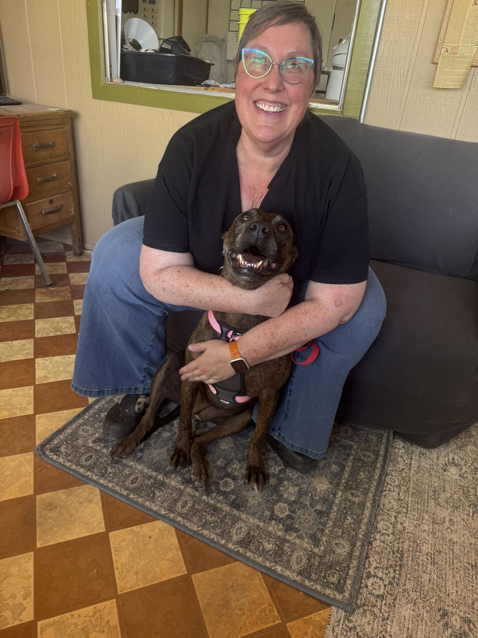 Woman smiling and holding a small black dog on a couch in a cozy living room