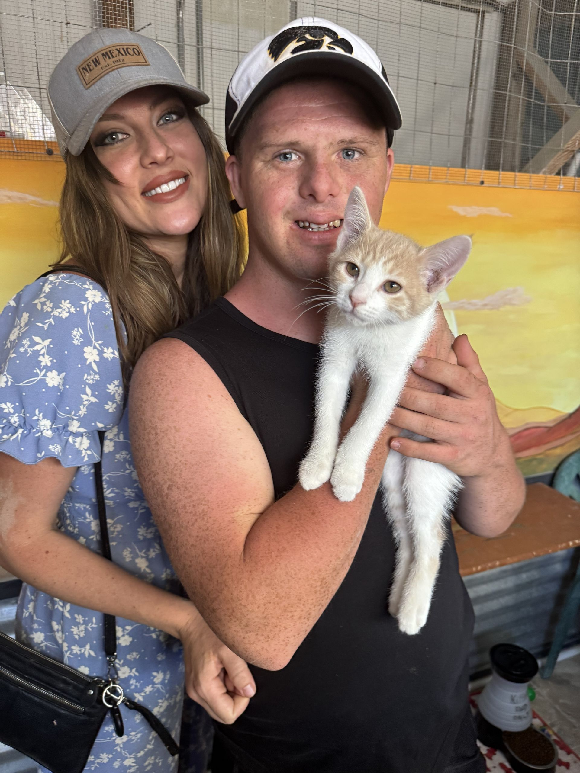 Two people smiling and holding a small white-and-orange kitten indoors