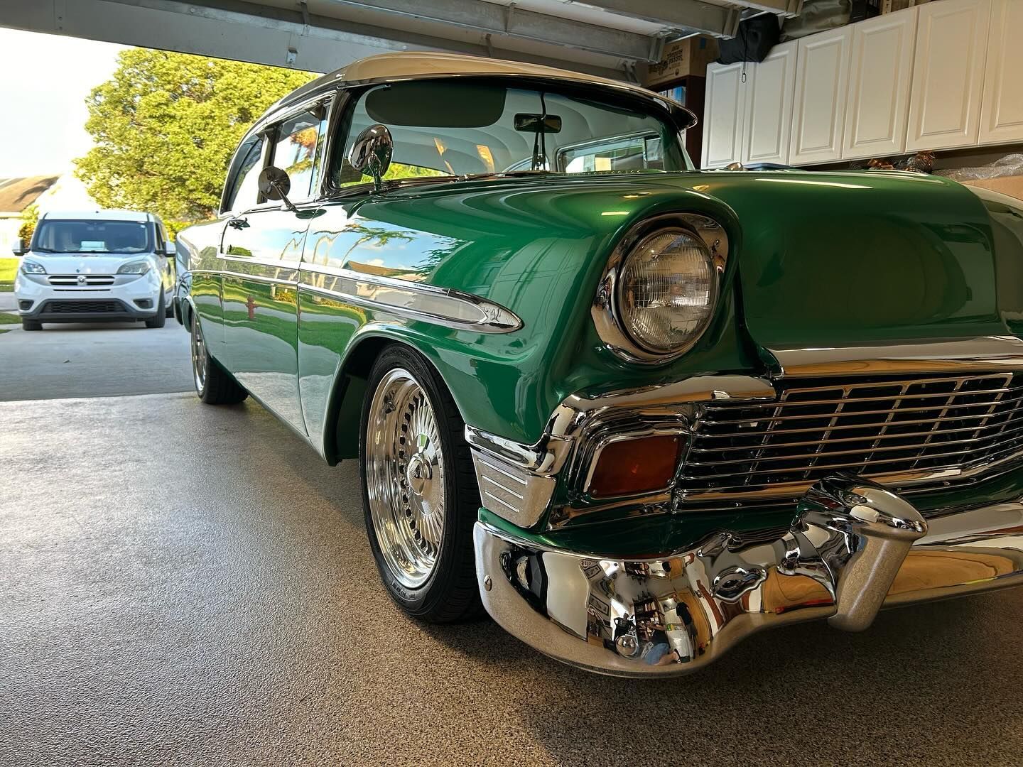 A green classic car is parked in a garage.