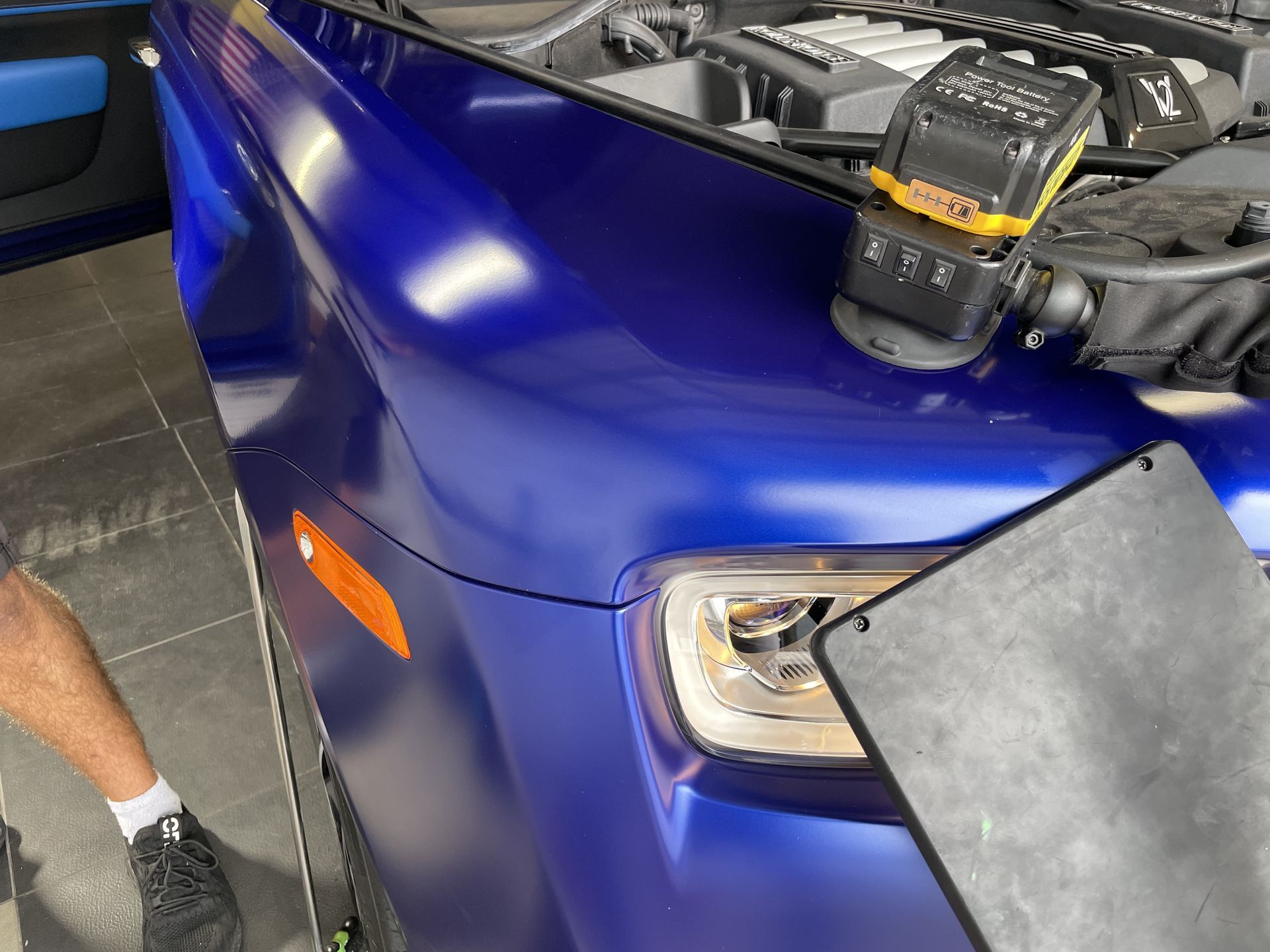 A man is working on a blue car with the hood open