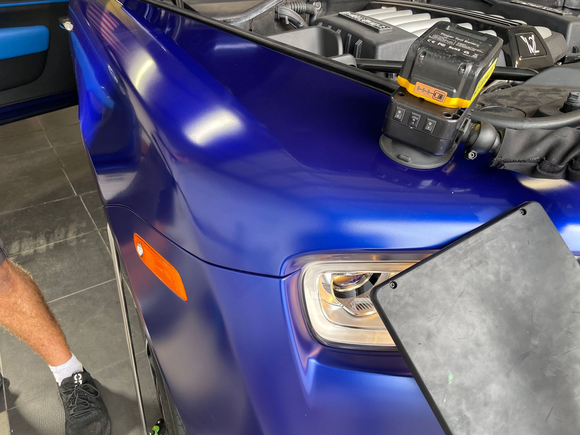 A man is standing next to a blue car with the hood open.