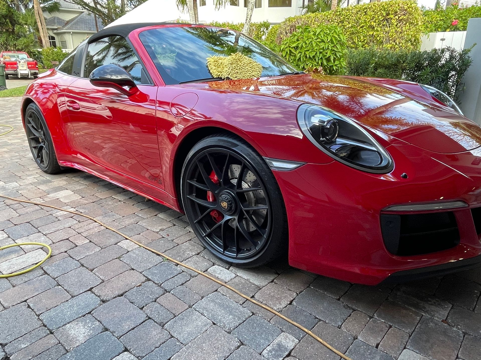 A red porsche 911 cabriolet is parked on a brick driveway.