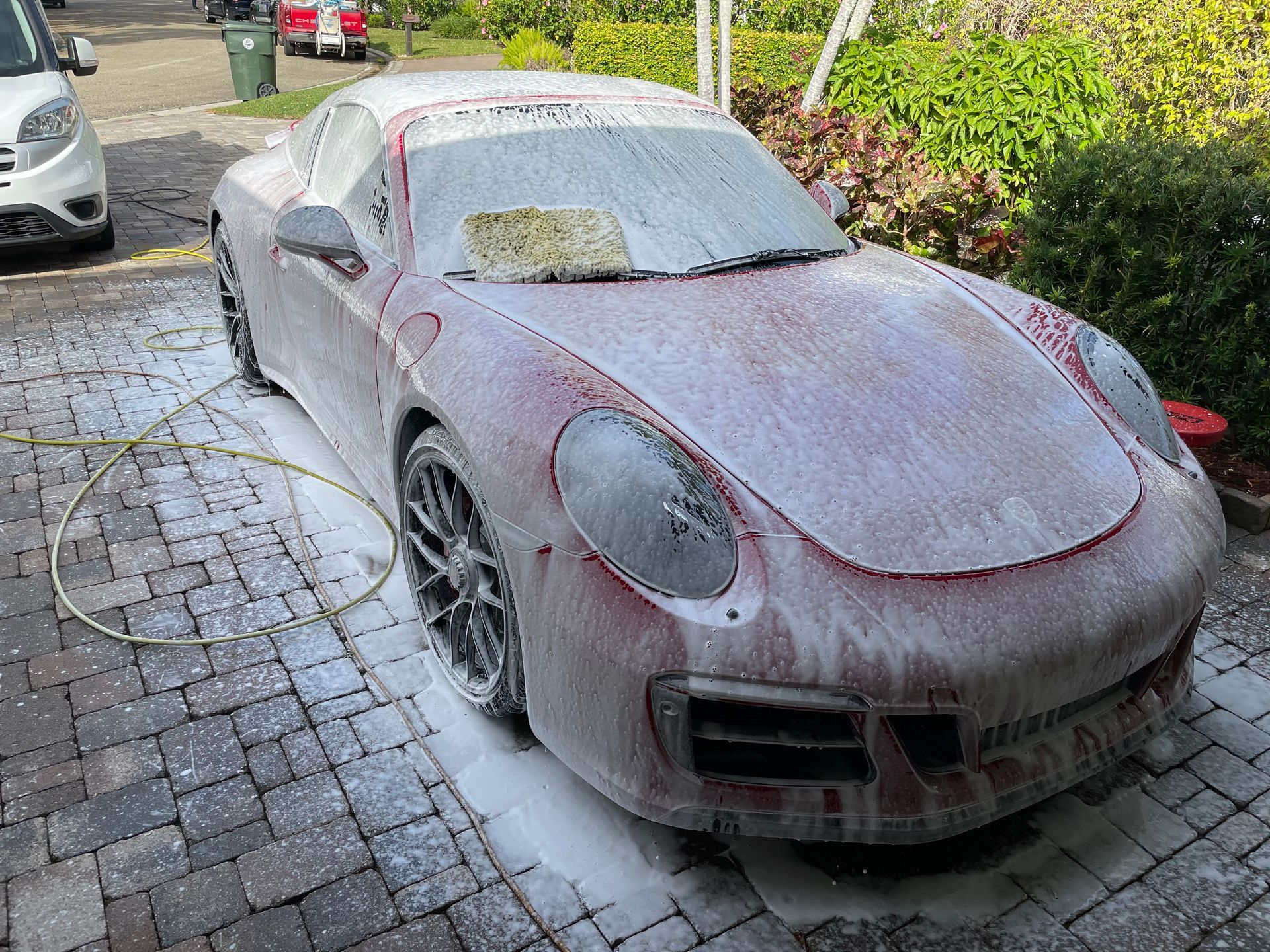 A car is covered in foam and is sitting on a brick driveway.