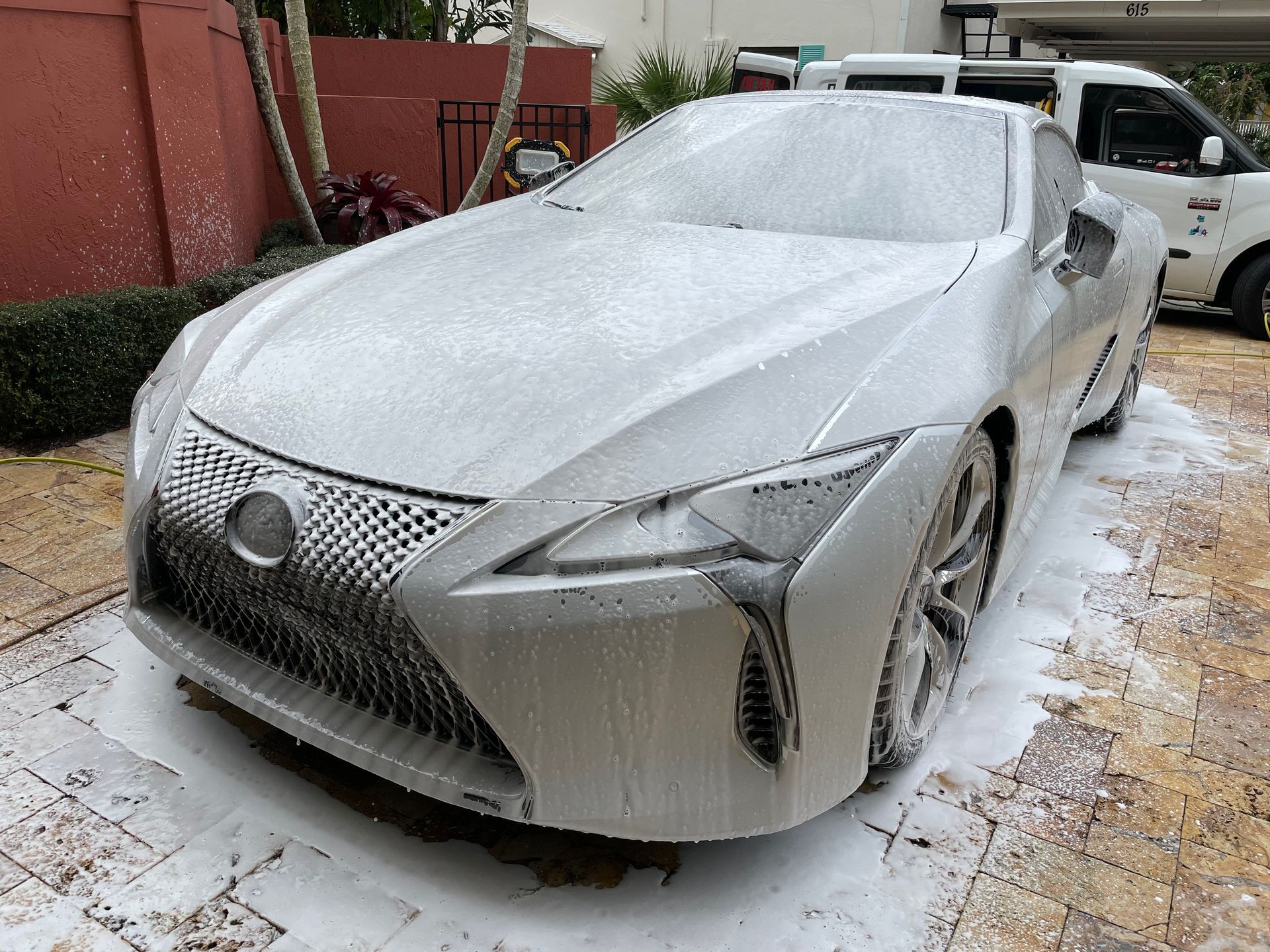A white car is covered in foam in a driveway.