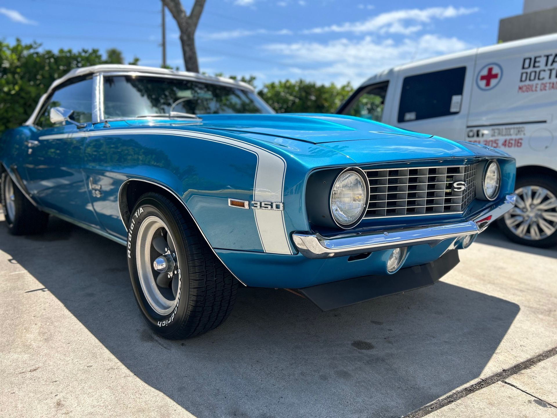 A blue and white car is parked in a parking lot next to an ambulance.