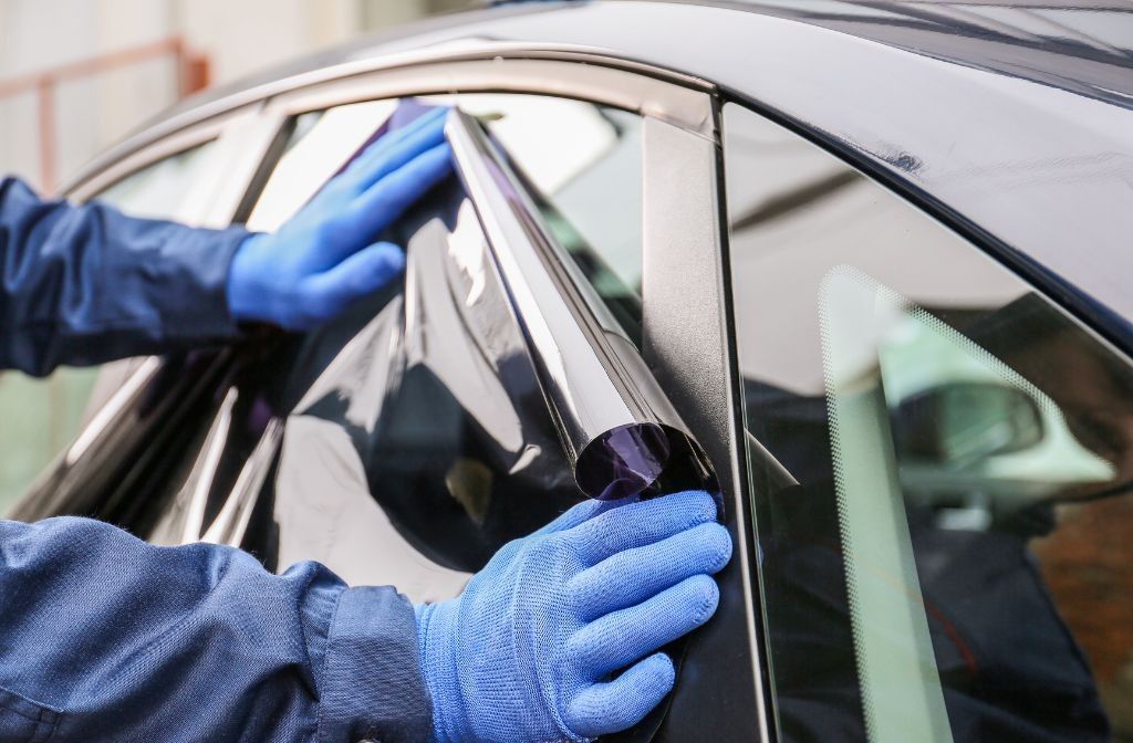 A person is applying tinted window film to a car window.