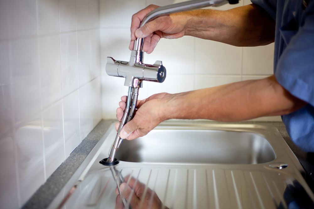 A man is fixing a faucet in a kitchen sink.