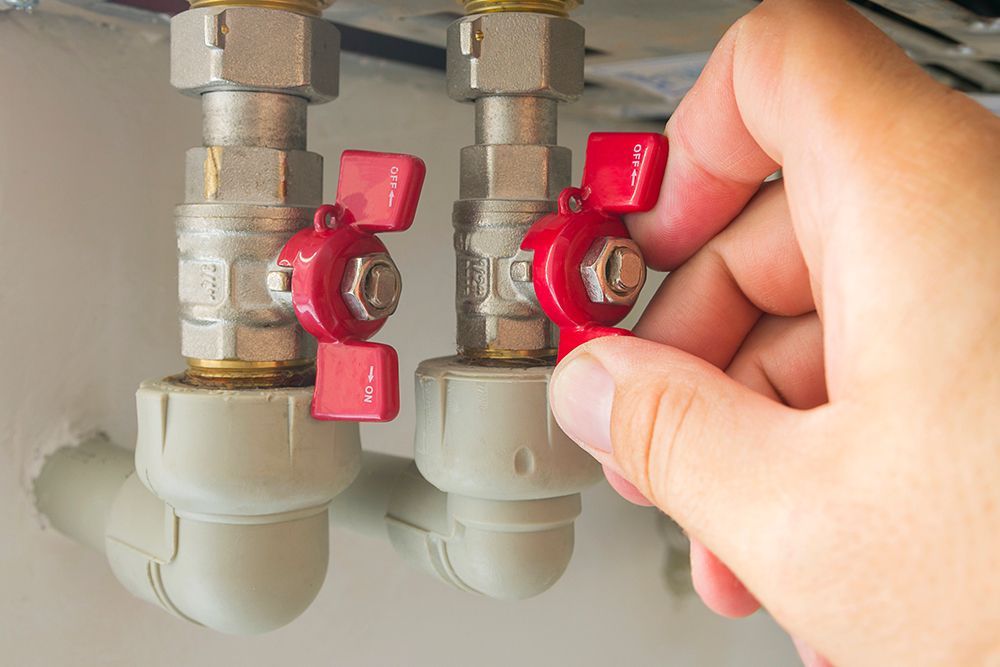 A person is holding a red valve on a pipe.