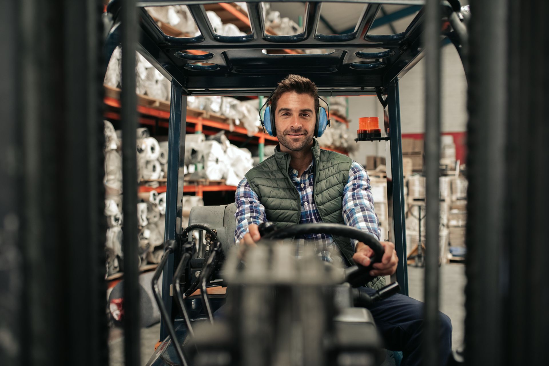 A man wearing headphones is driving a forklift in a warehouse.