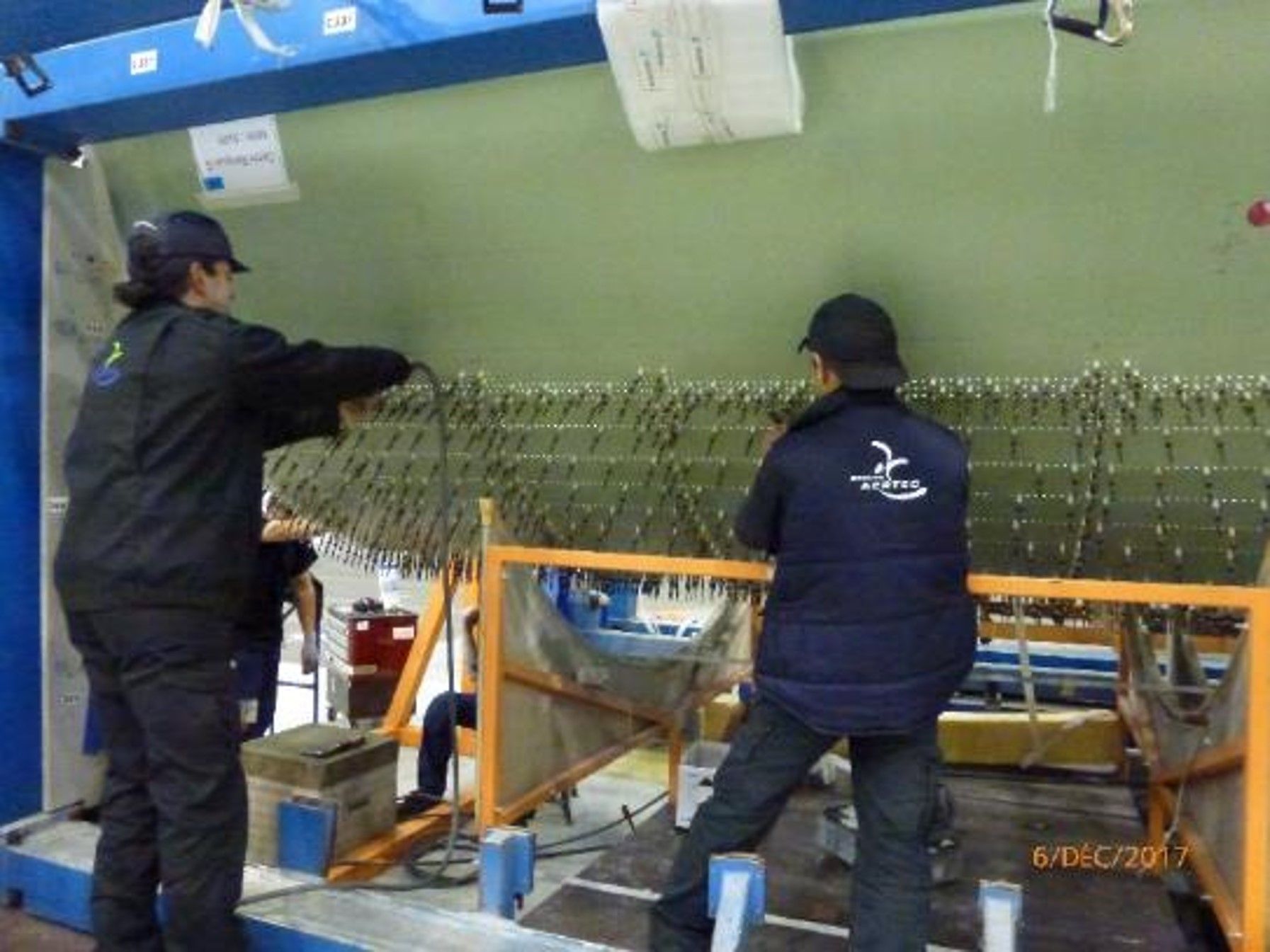 Deux personnes en tenue de travail noire assemblent des pièces sur une grande structure.