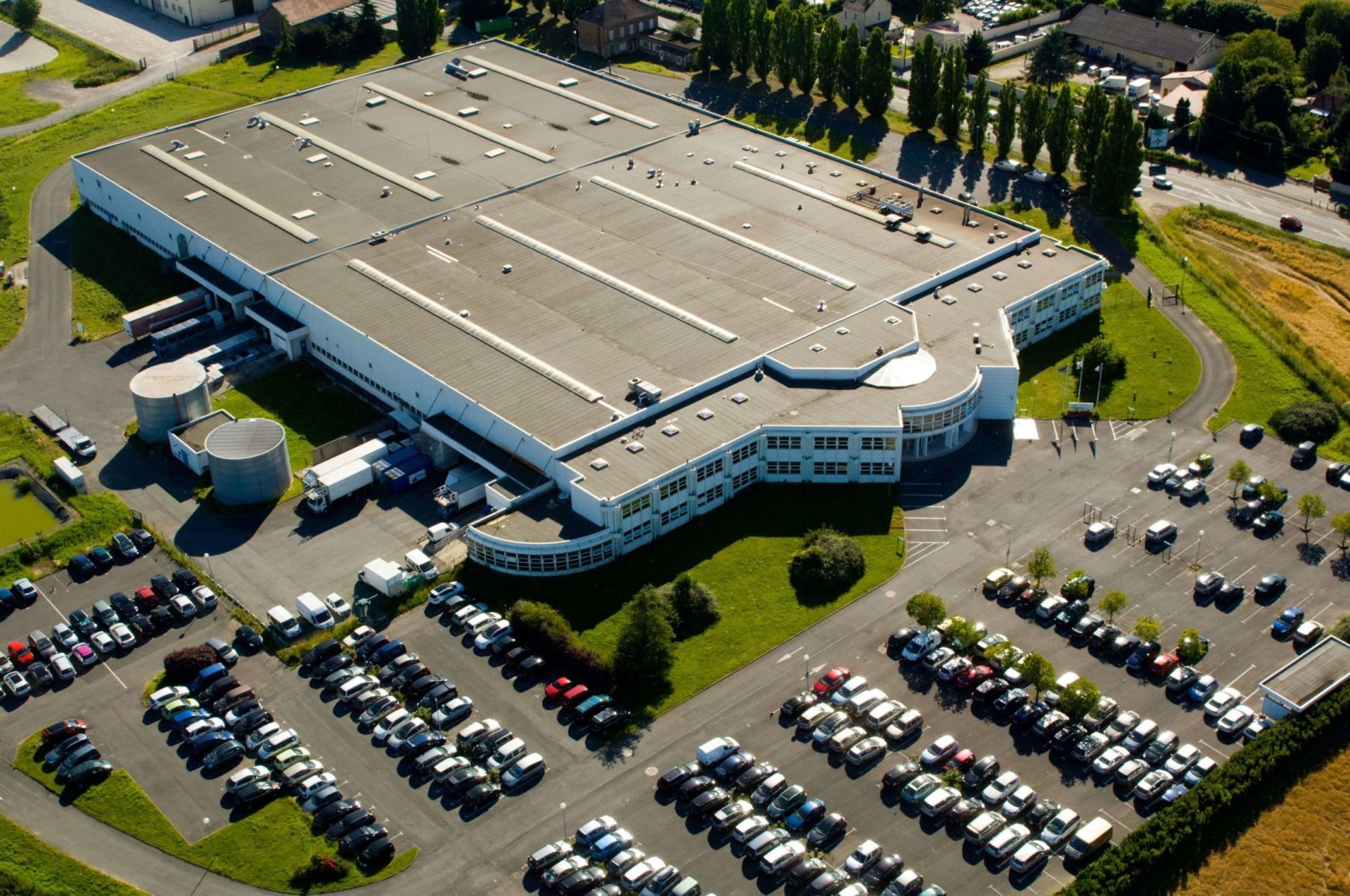 Vue aérienne d'un grand bâtiment industriel avec un vaste parking et des camions.