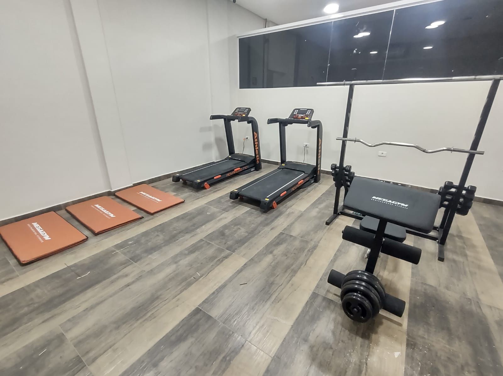 Uma academia com esteiras e uma barra no chão.