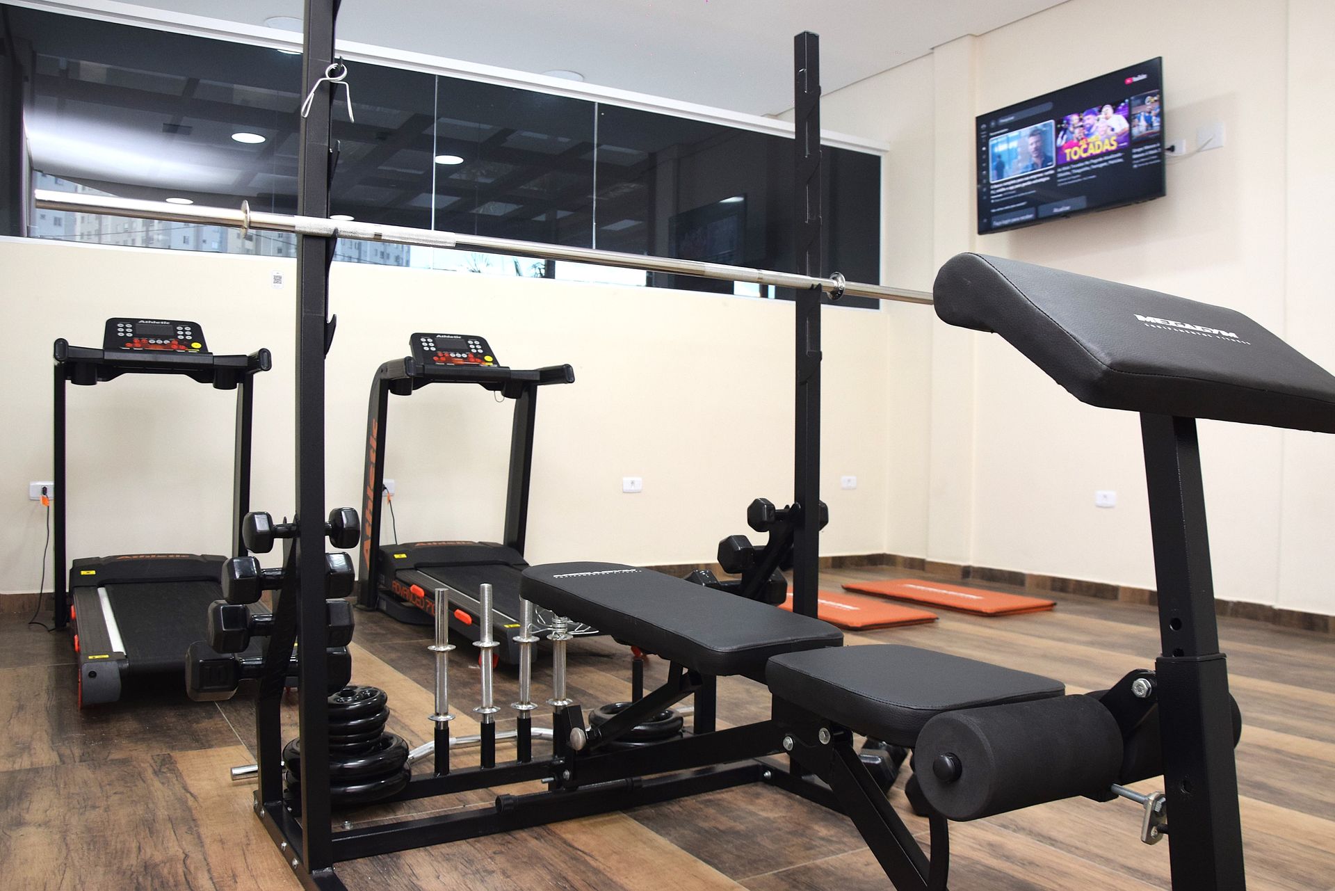 Uma academia com esteiras e uma barra no chão.