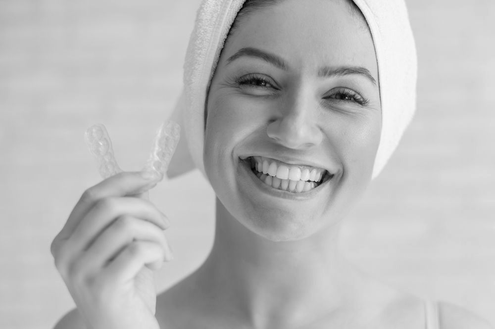 a woman with a towel wrapped around her head is smiling while holding clear braces.