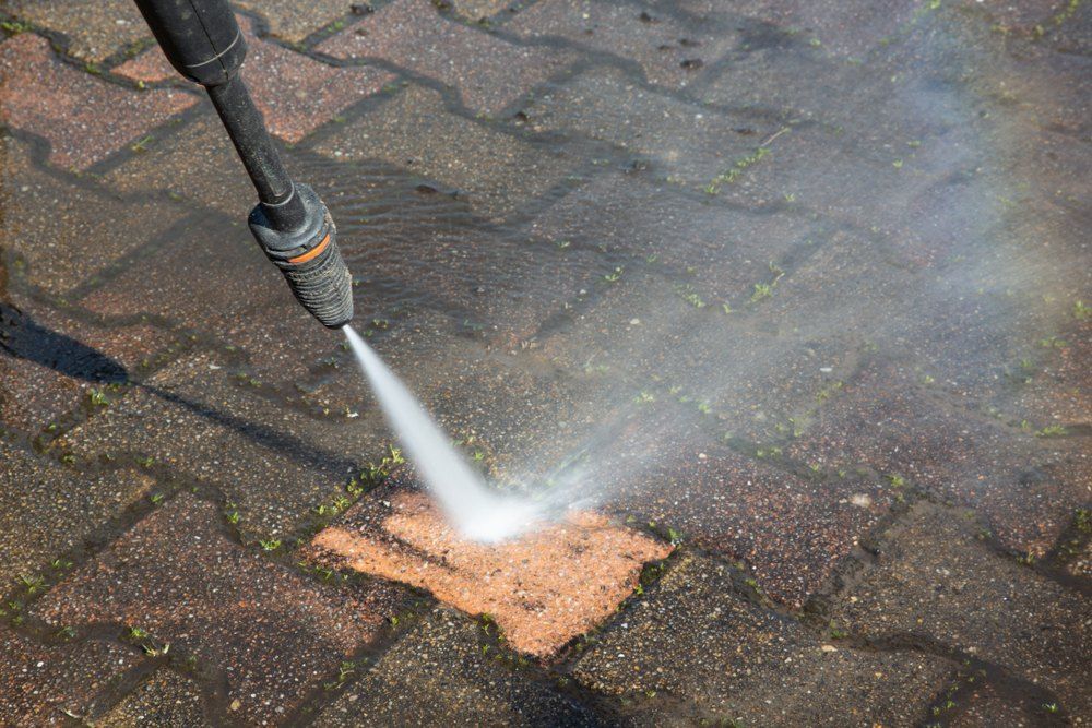 A Person is Using a High Pressure Washer to a Brick Walkway — EDU-BABA Pressure Cleaning in Evatt, ACT
