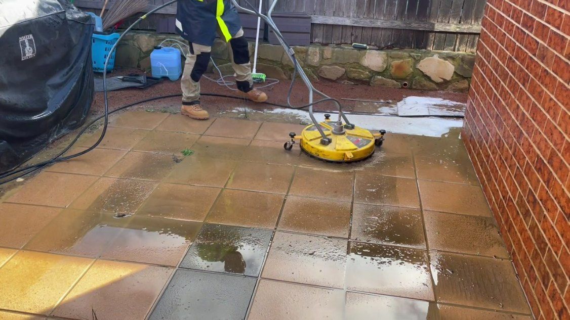 A Person is Cleaning a Patio With a Machine — EDU-BABA Pressure Cleaning in Weston Creek, ACT