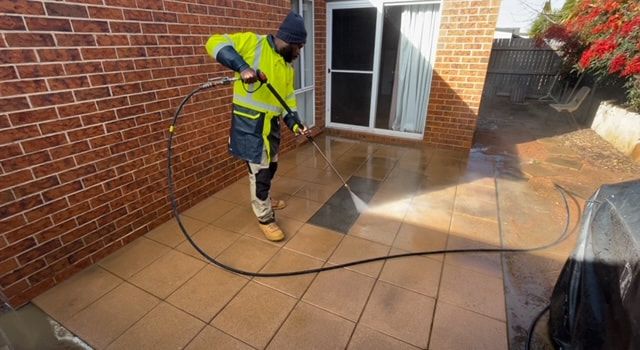 A Worker in An Orange Vest Sprays Water on A Wet, Gray Sidewalk with A Hose — EDU-BABA Pressure Cleaning in Gungahlin, ACT