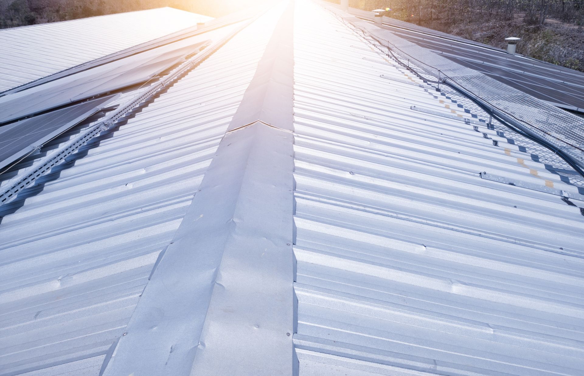 Metal roof reflecting sunlight, with long angled panels converging towards a central ridge.