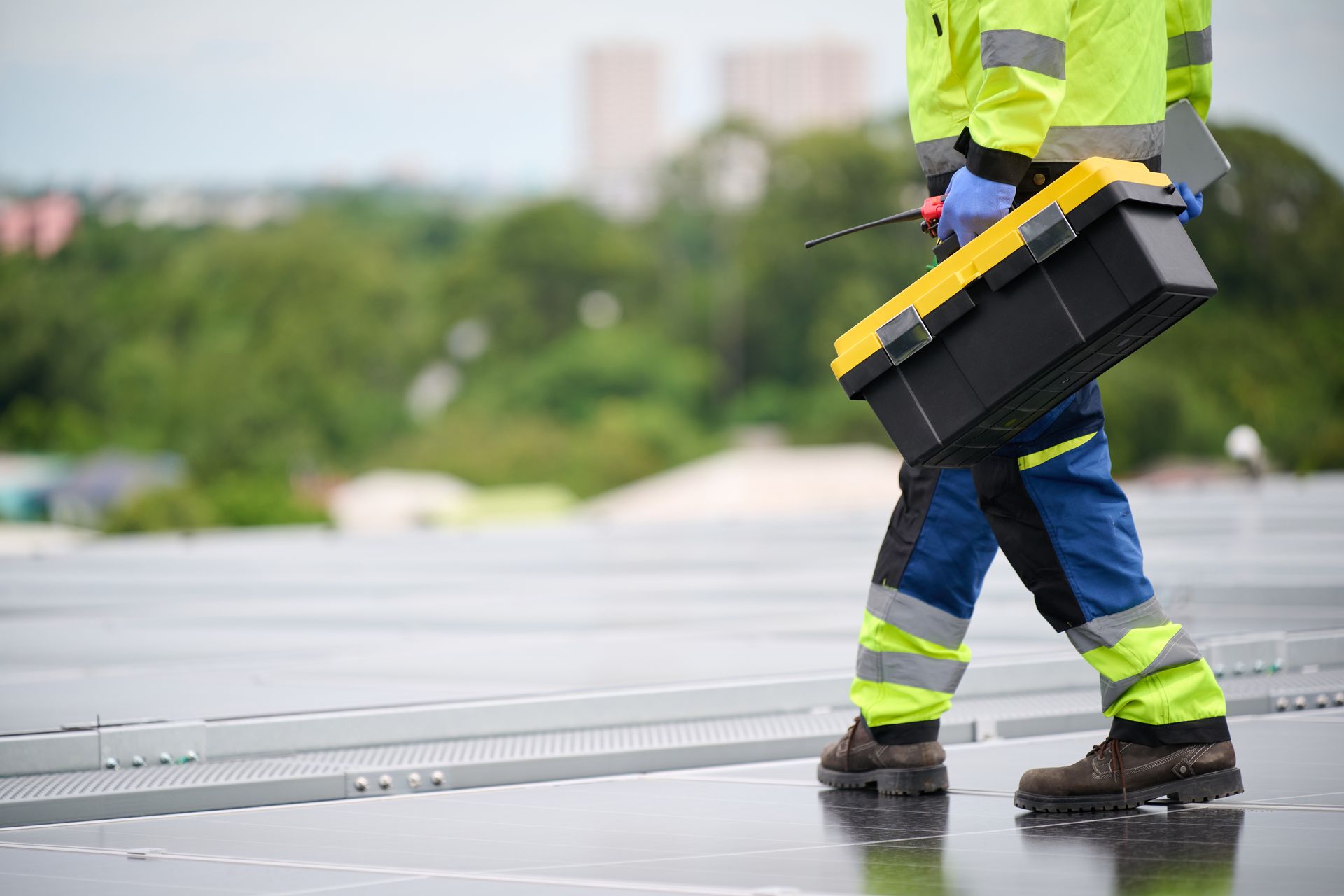 Construction worker in reflective gear walking on solar panels, carrying a toolbox.