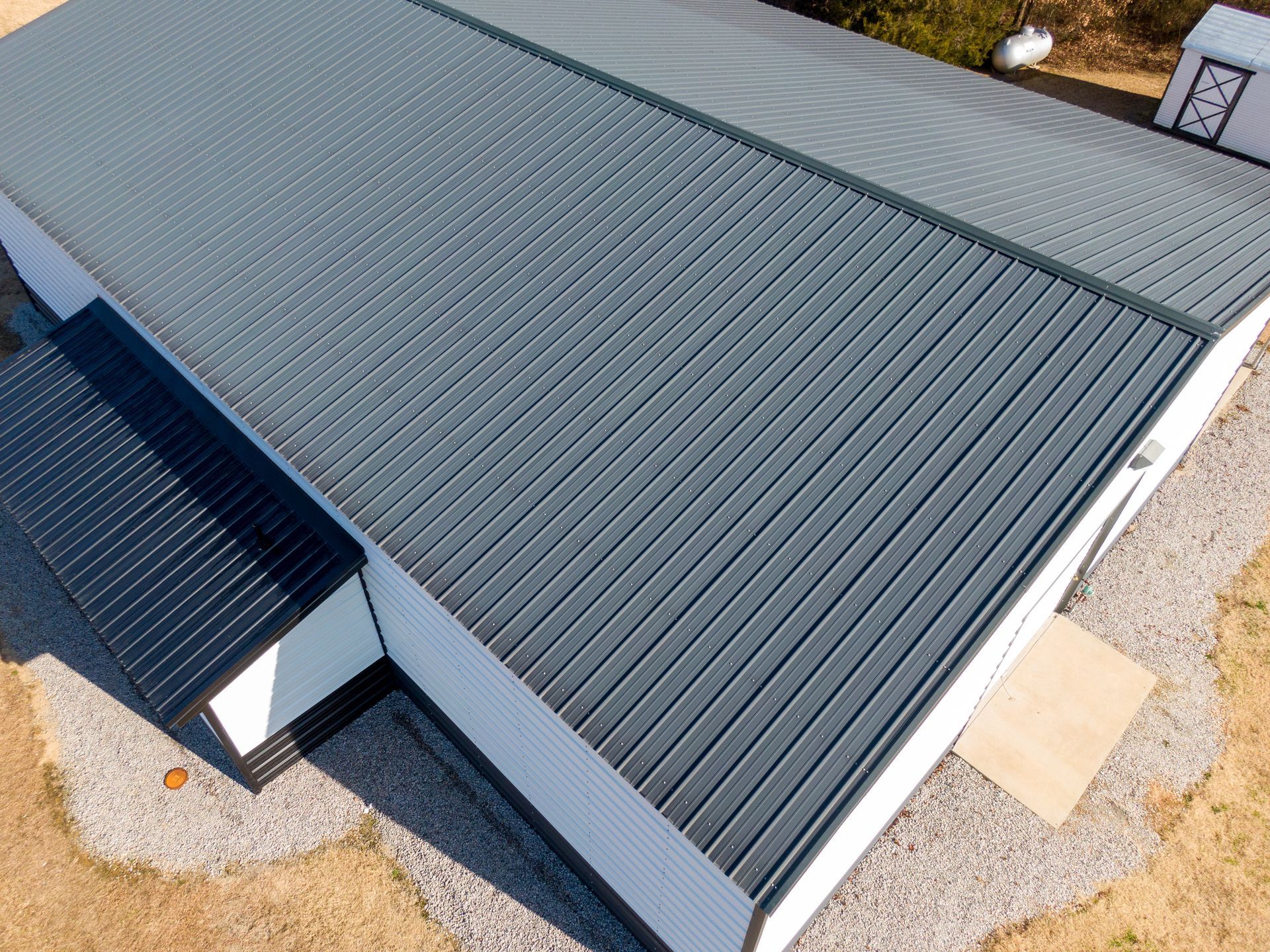 Gray metal roof on a white building, gravel surrounding the base, bright sunny day.