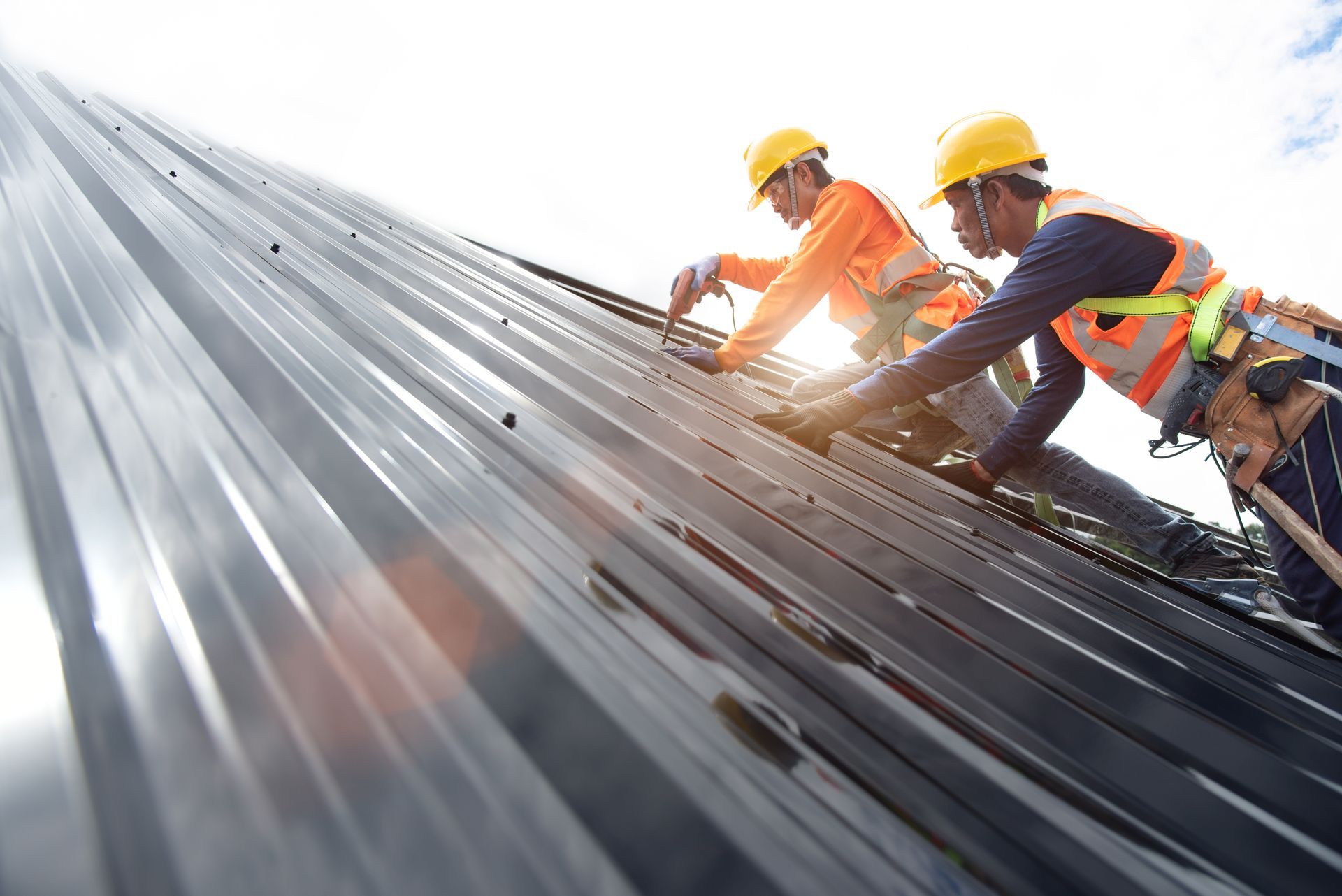 Two roofers in hard hats and safety gear installing metal panels on a rooftop.