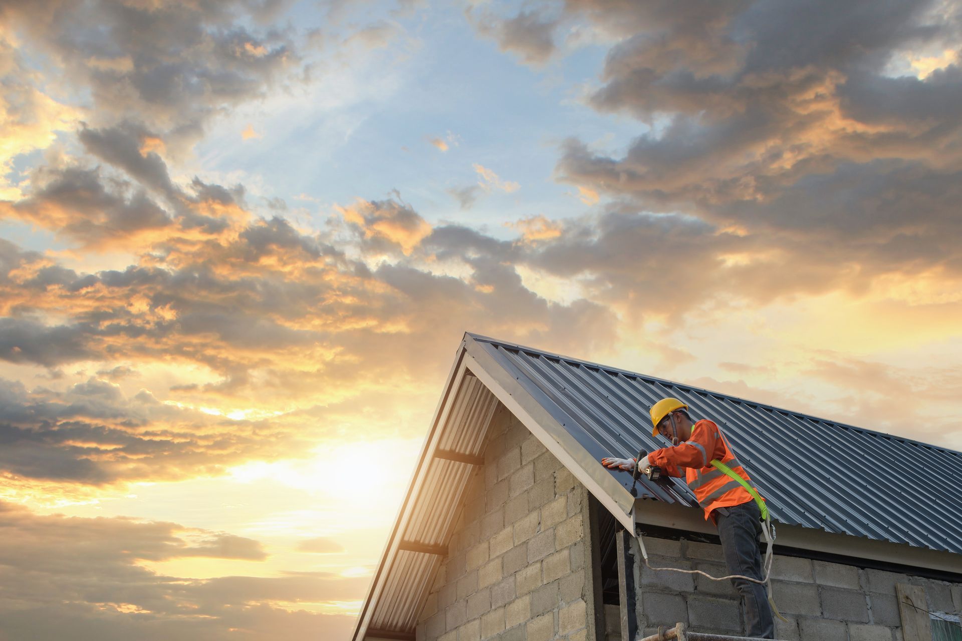 Roofer on a roof, attaching metal panels. Sunset sky background.