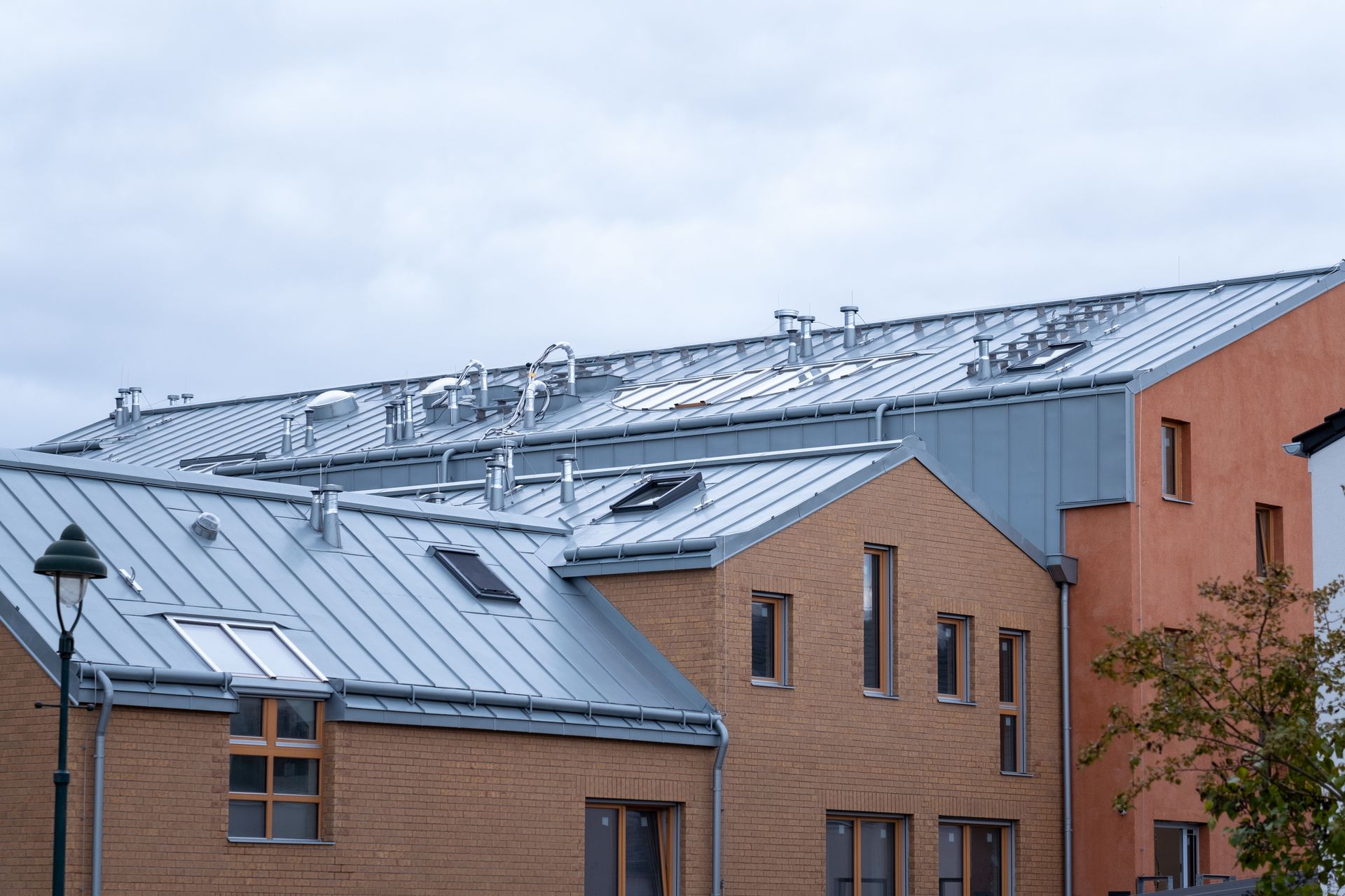 Buildings with metal roofs and various chimneys against a cloudy sky.