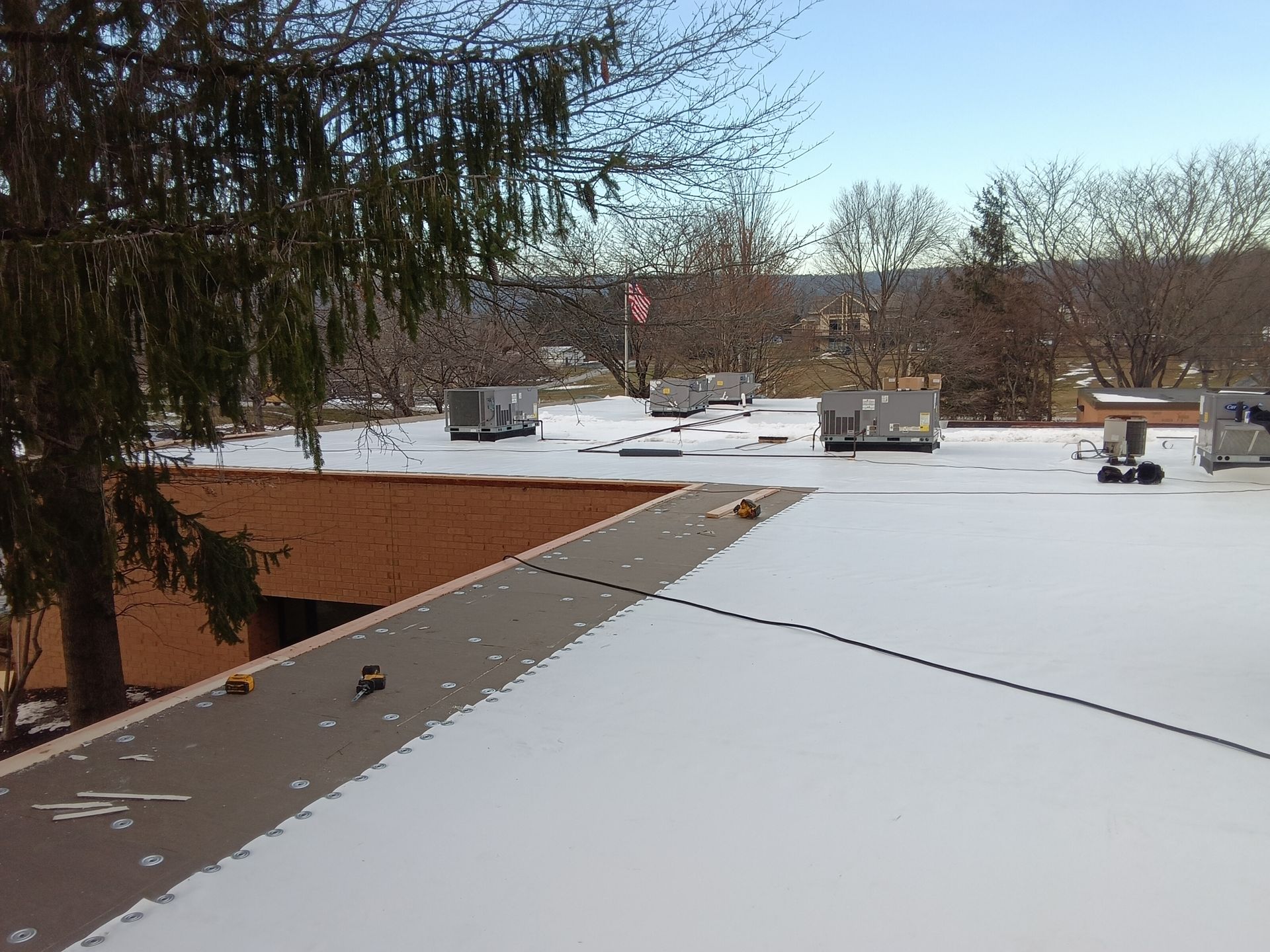 Roofer wearing an orange safety harness working on a flat, dark roof, near a skylight. Roofer wearing an orange safety harness working on a flat, dark roof, near a skylight.