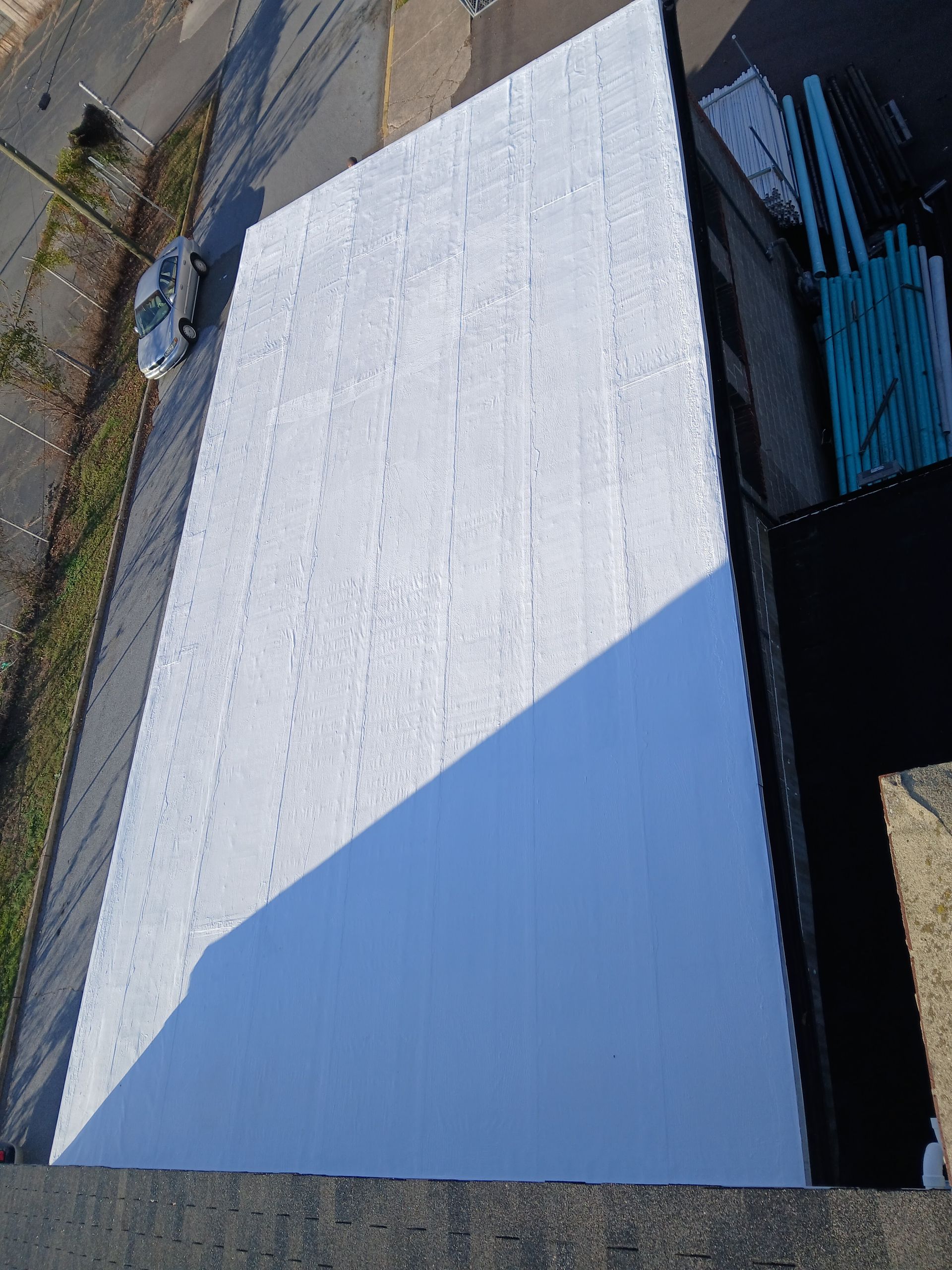 Roofer in red cap on flat roof, installing dark material. Tools visible. Building has wood siding.