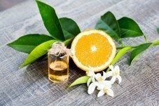Orange slice with green leaves, white flowers, and a small bottle of essential oil on a gray cloth.
