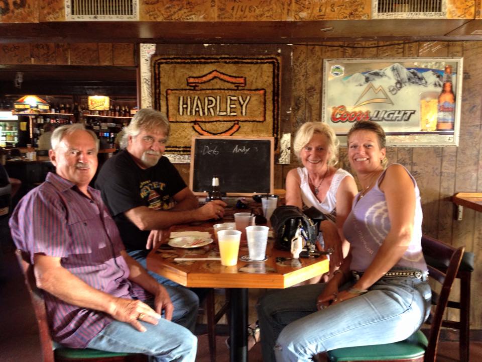 A group of people sit at a table in front of a harley davidson sign