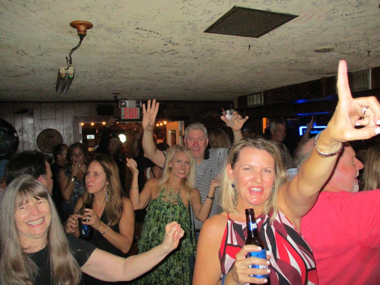 A group of people are dancing in a room with an exit sign in the background
