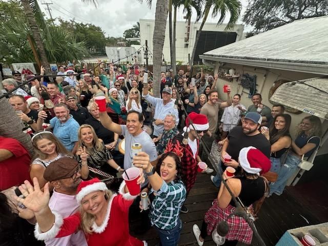A large group of people wearing santa hats are standing in front of a house.