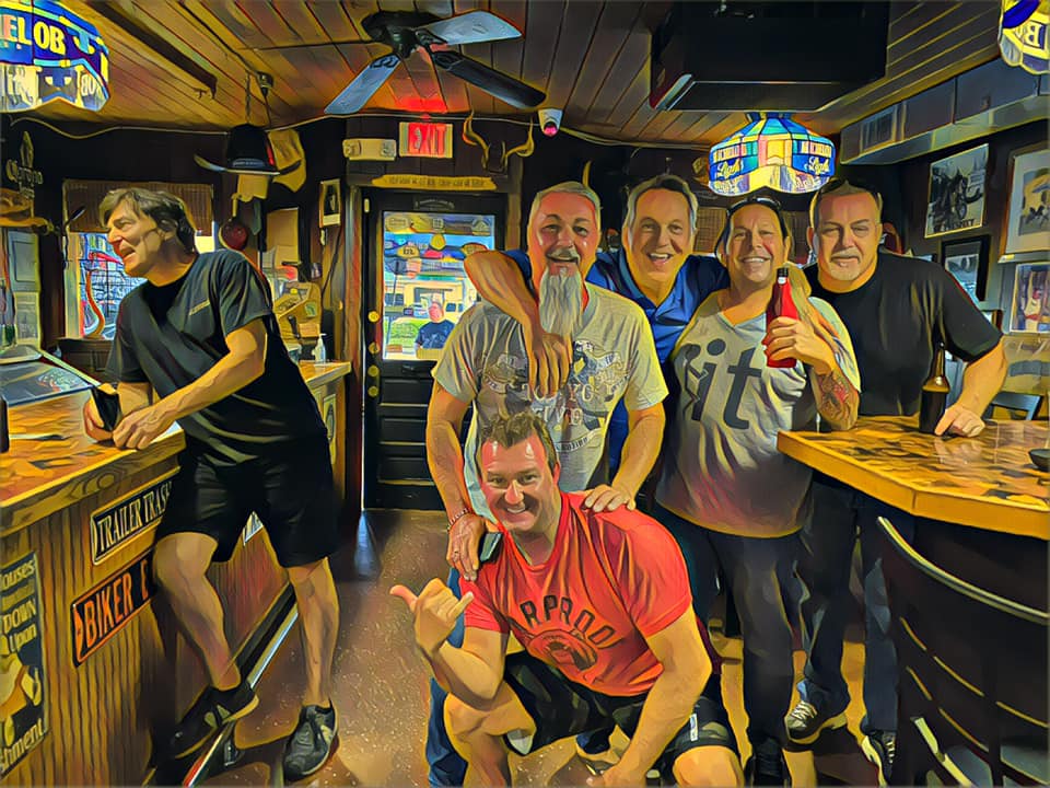 A group of men are posing for a picture in a bar with a sign that says exit