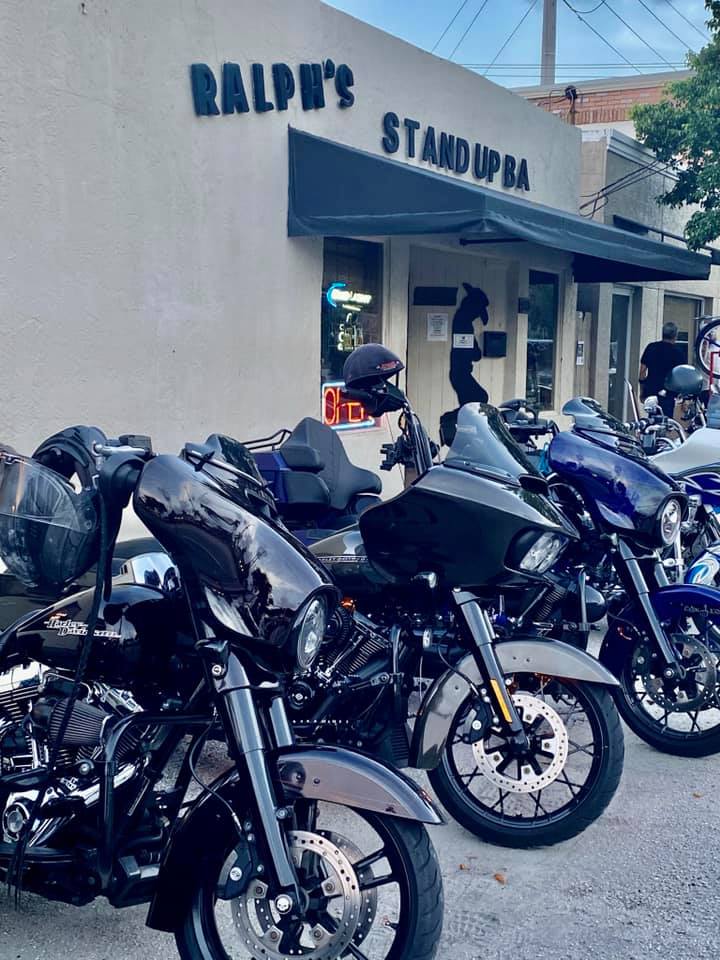 A row of motorcycles parked in front of ralph 's stand up bar