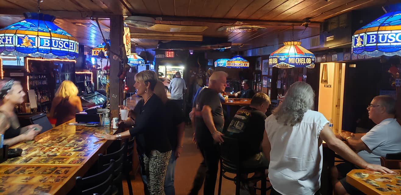 People sitting at tables in a bar with a bud light sign