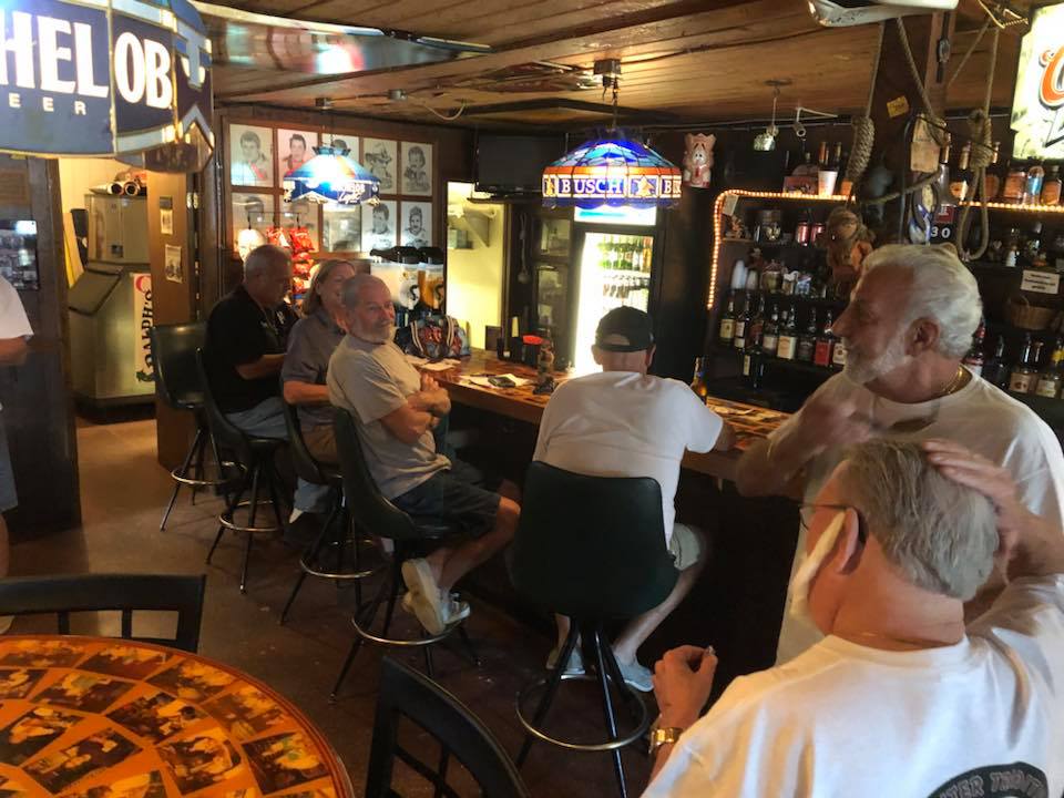 A group of men sit at a bar under a sign that says helo8