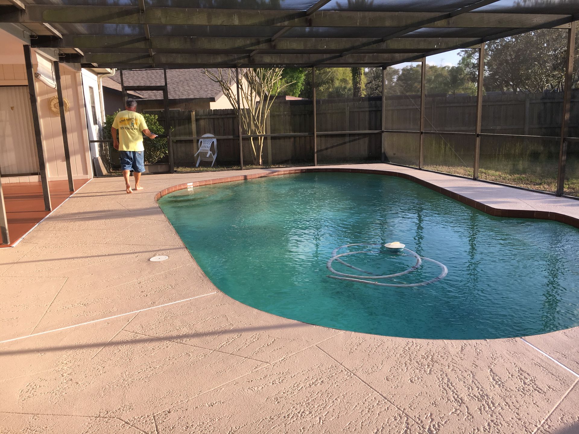 Person walks on a patio next to a turquoise swimming pool enclosed by a screened-in lanai.