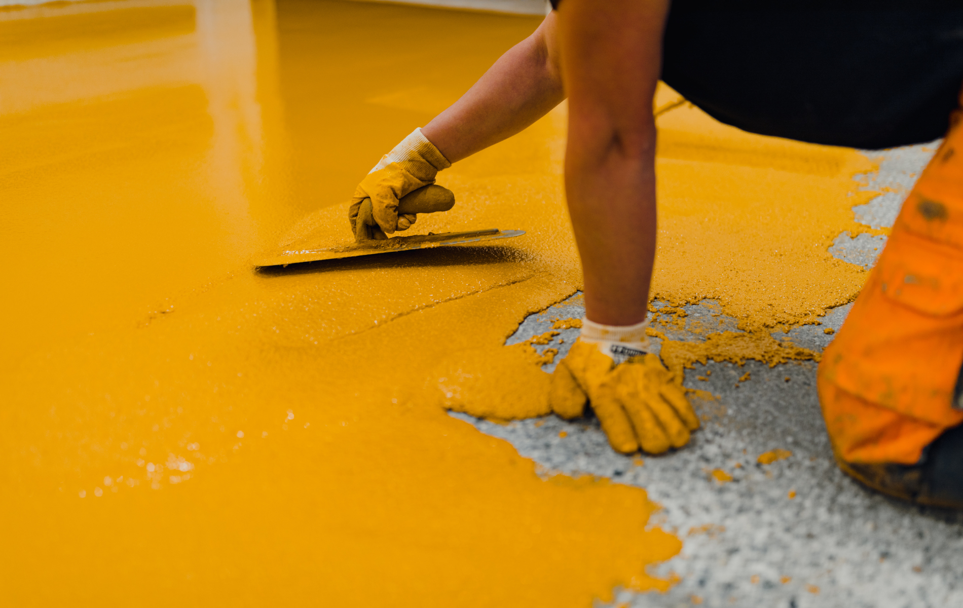 Person using a trowel to spread yellow epoxy flooring on a concrete surface.