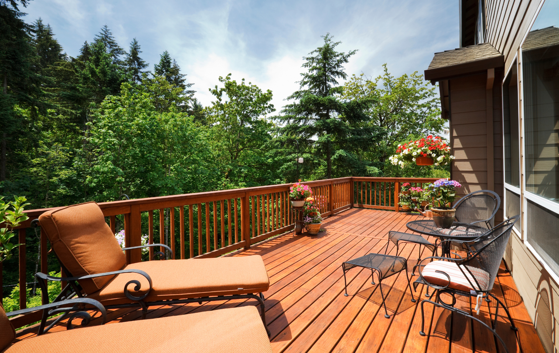 Wooden deck with lounge chair and table, overlooking trees; brown and green colors.