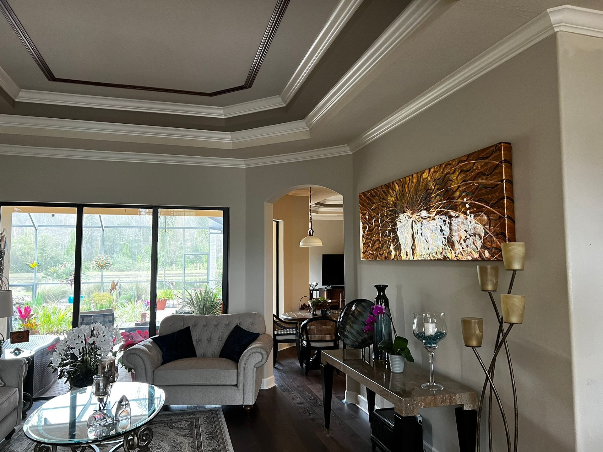 Living room with ornate crown molding, large artwork, and view of a patio.